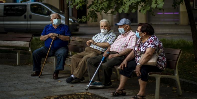 Elderly people wearing face masks sit on a bench in a square in Barcelona.  (Photo: Al Jazeera) 